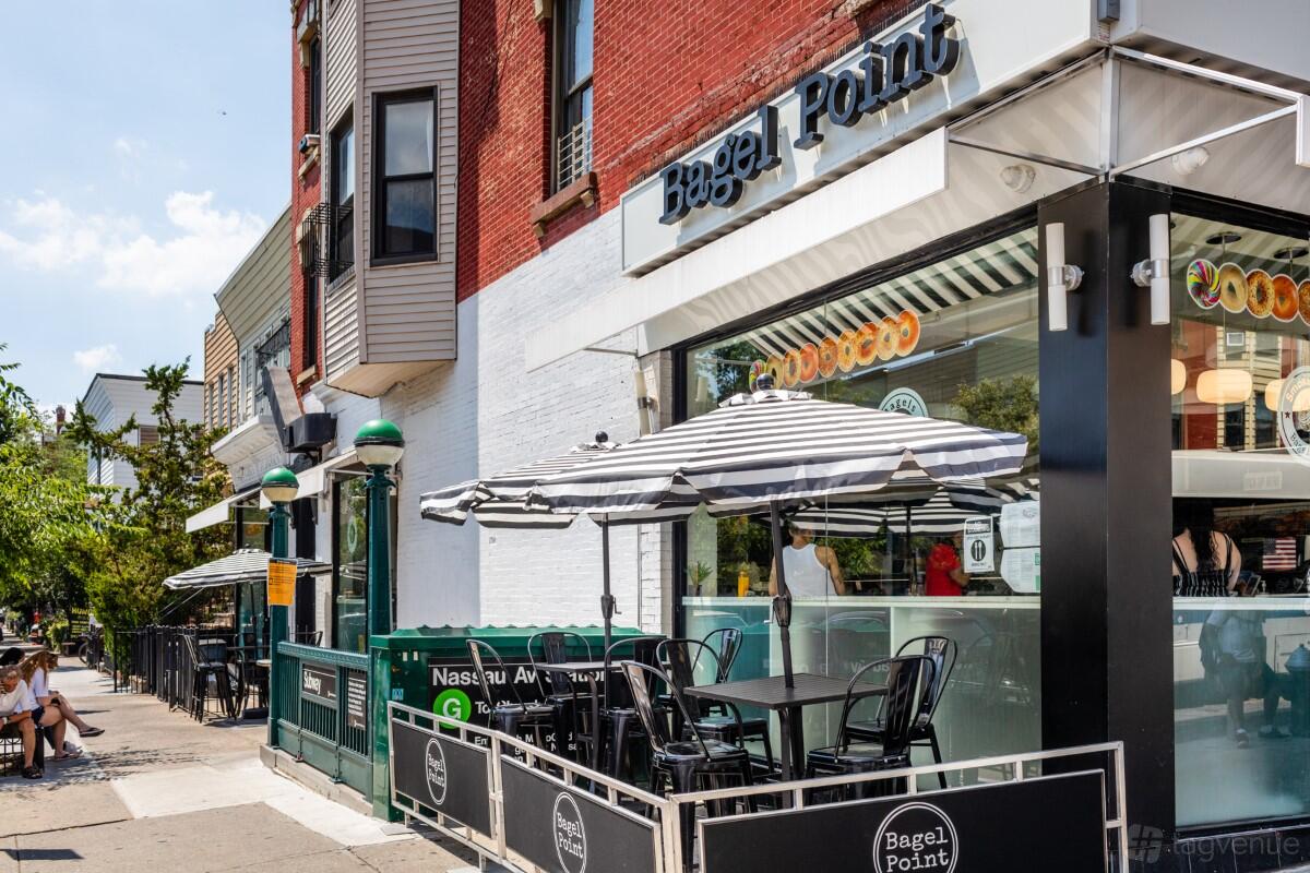 A restaurant patio with black tables, striped umbrellas, and sidewalk seating at Bagel Point.