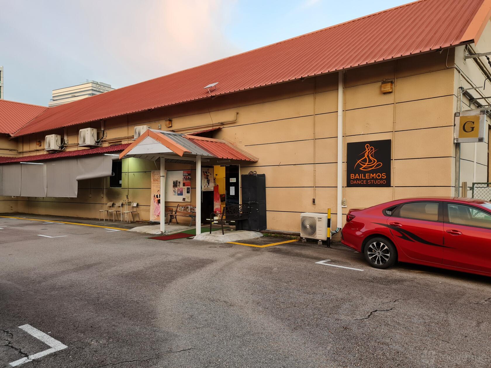 A versatile event space with tan exterior walls, red metal roof, and Bailemos Dance Studio signage at Bailemos Studio.