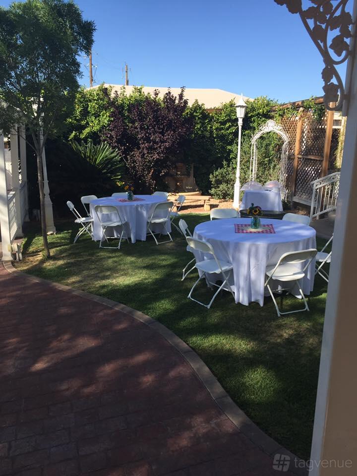 A church garden with round tables draped in white linens and folding chairs set on grass at Little Chapel on the Corner.