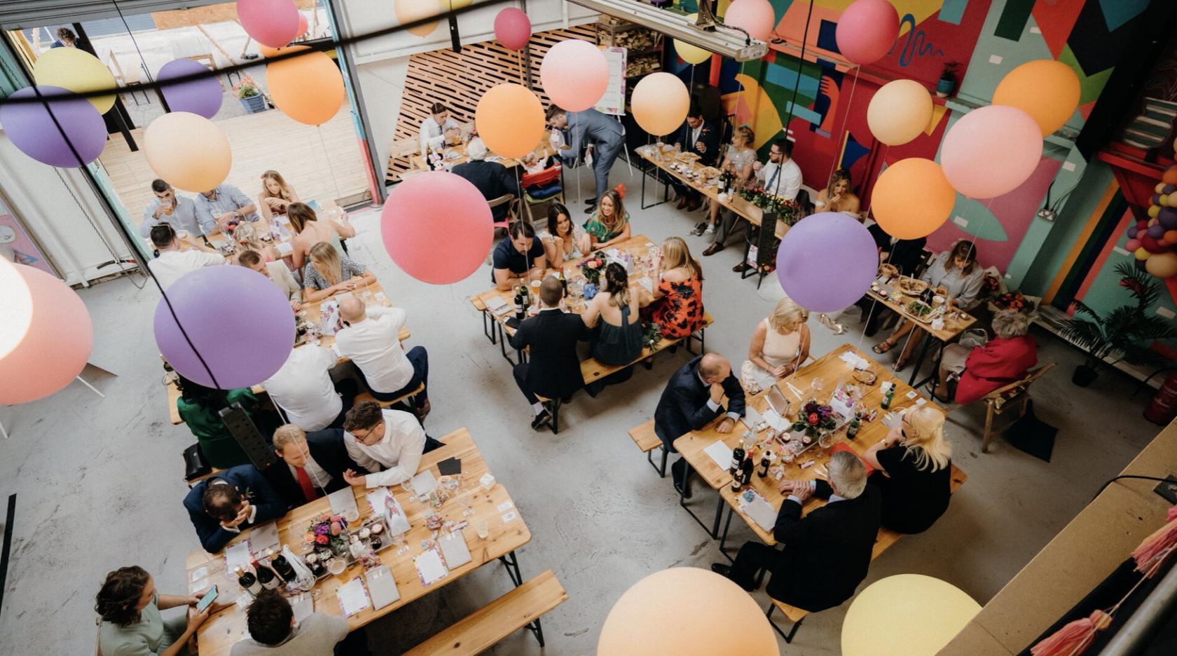 An event venue with long wooden tables, colorful balloons, and a mural wall at Bloom Building.