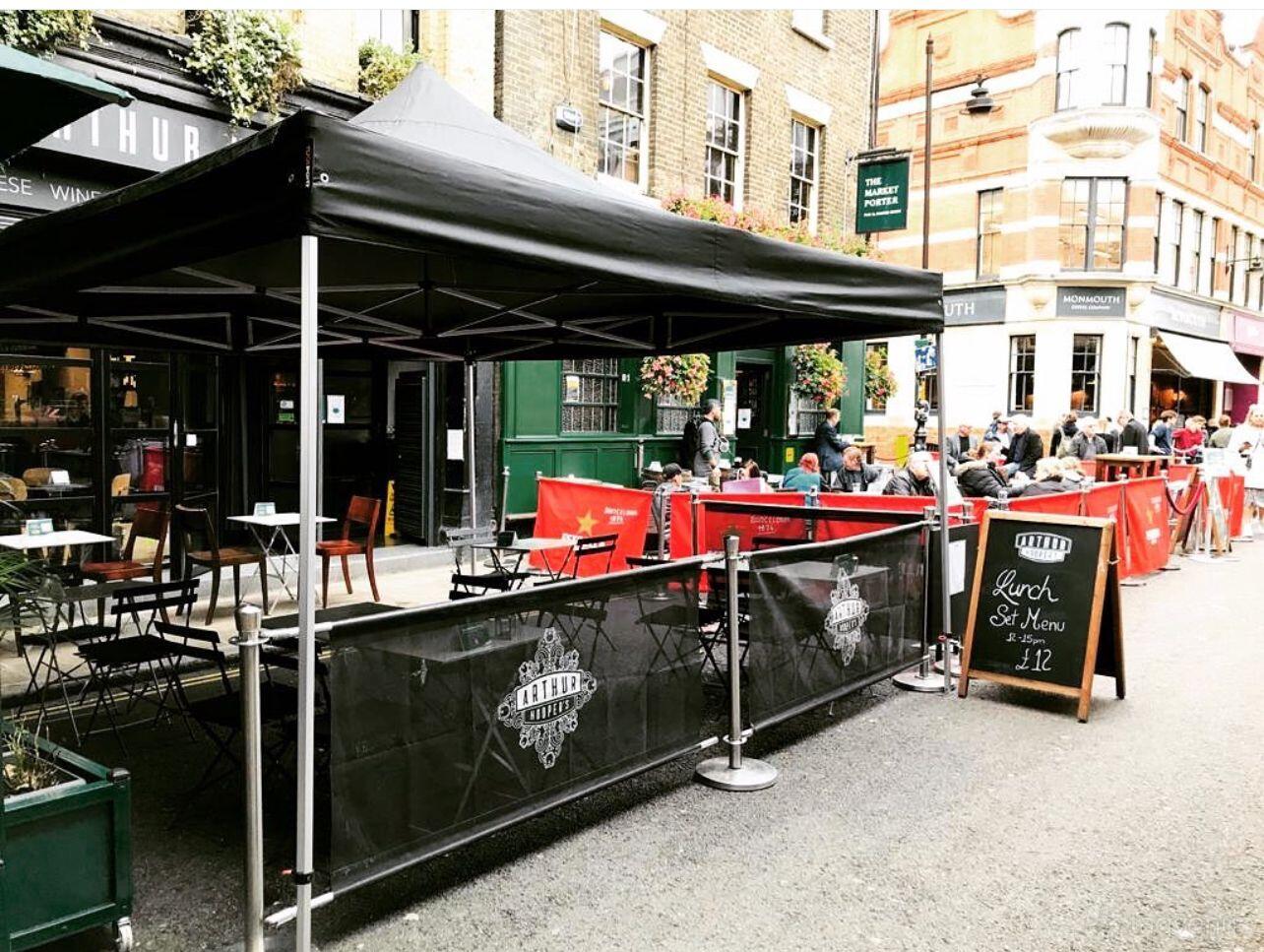 A restaurant terrace with covered tables, black fencing, and a street menu board outside Arthur Hooper's.