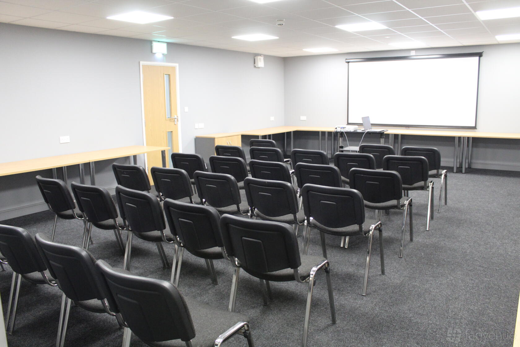 A meeting room with rows of black chairs, a projector screen, and wall-mounted tables at Avon Lodge.