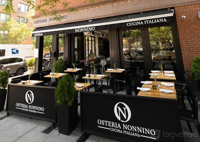 A restaurant with outdoor tables, black planters, and an awning with Italian signage at Osteria Nonnino.