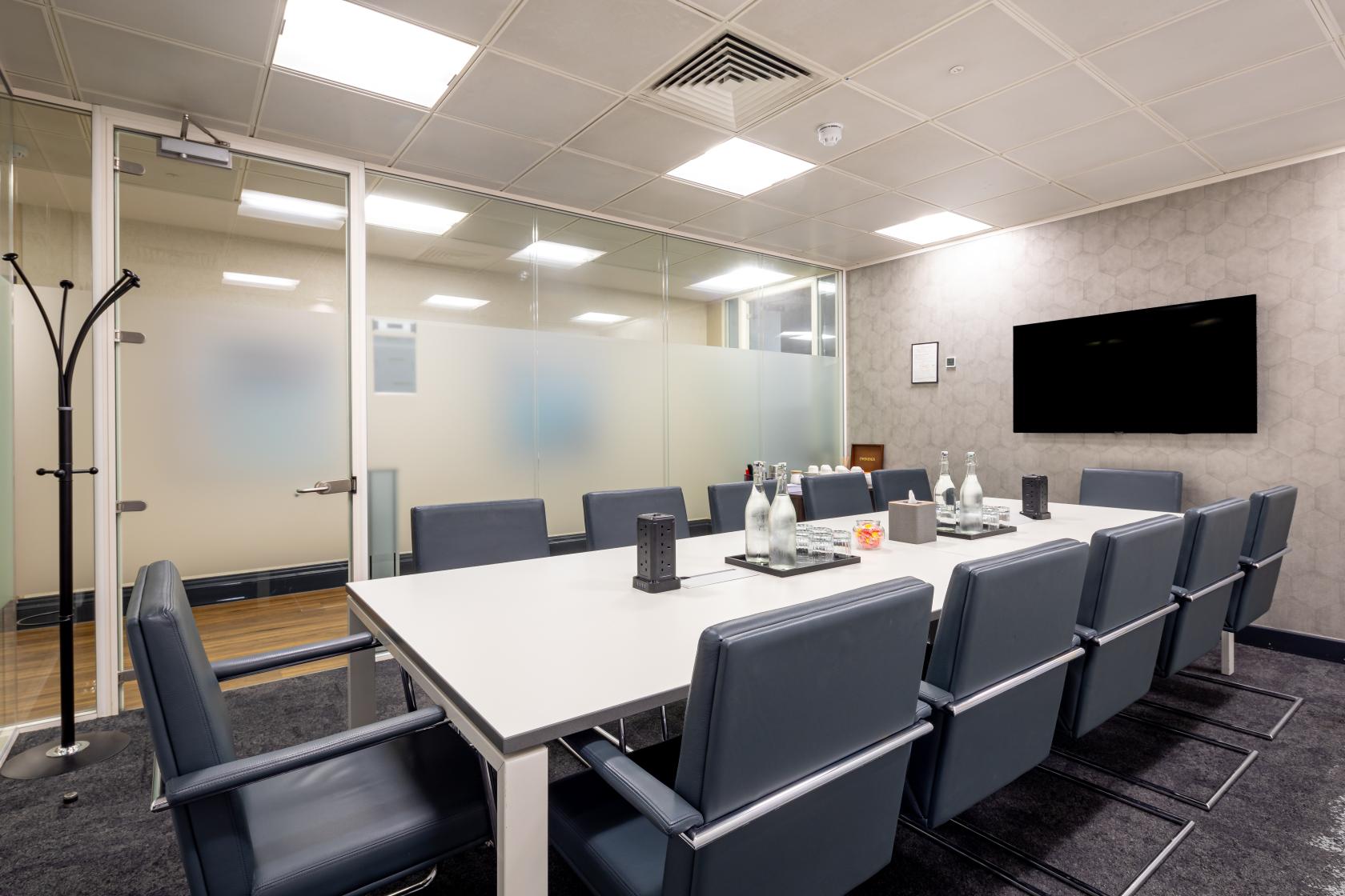 A meeting centre with a long rectangular table, leather chairs, glass wall, and a mounted screen at Landmark: Royal Exchange, Bank, London.