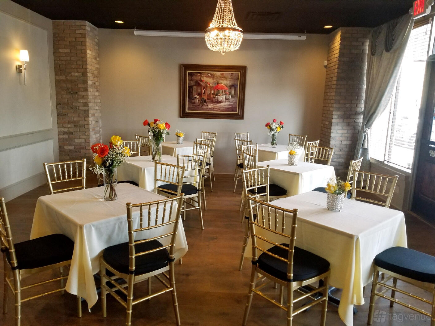 A dining room with gold chiavari chairs, square tables with white linens, and a chandelier at New Season Catering.