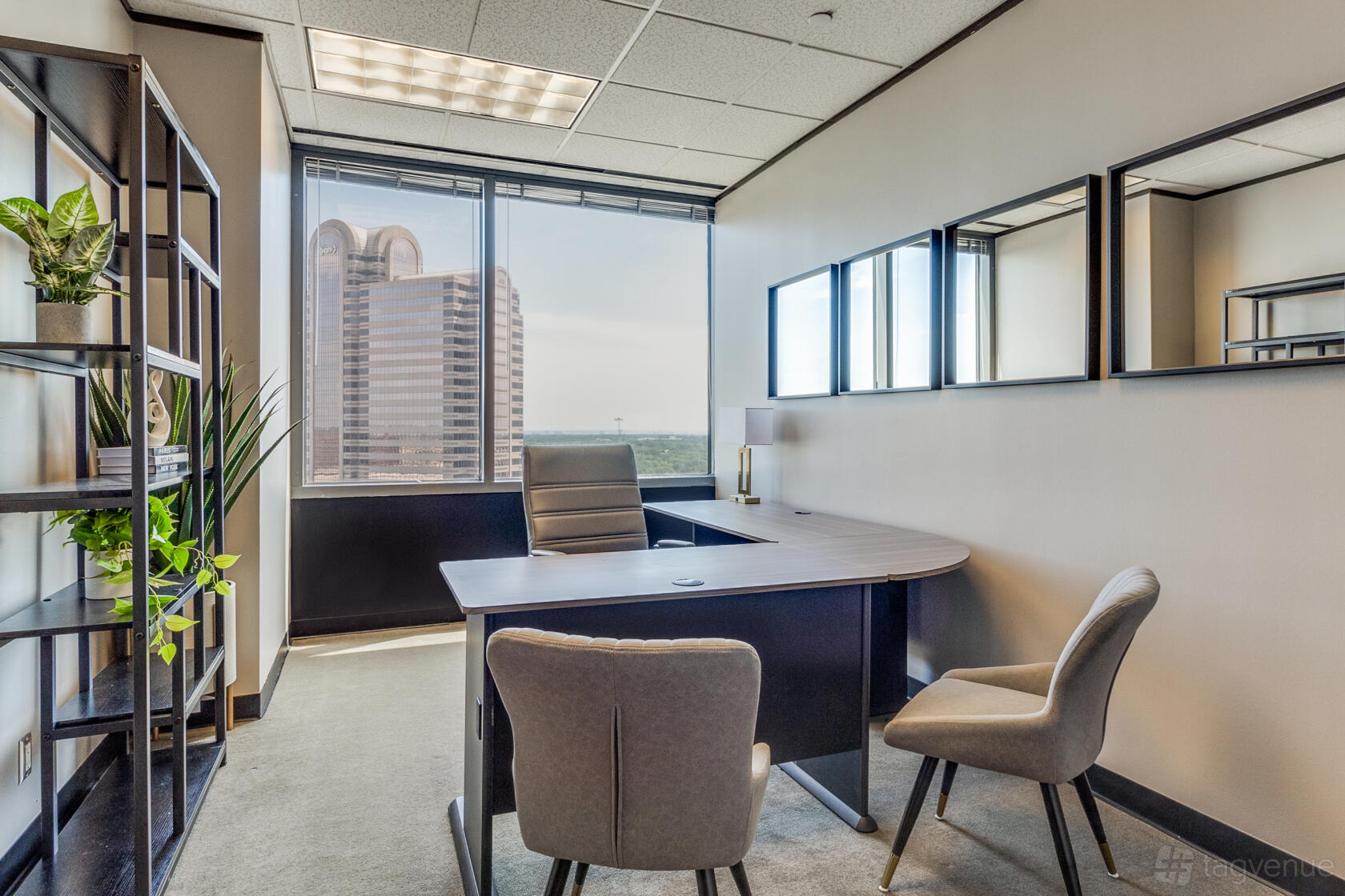 An office space with a large desk, two gray chairs, wall mirrors, shelving, and a window overlooking the city at Lucid Private Offices - Galleria Addison T1.