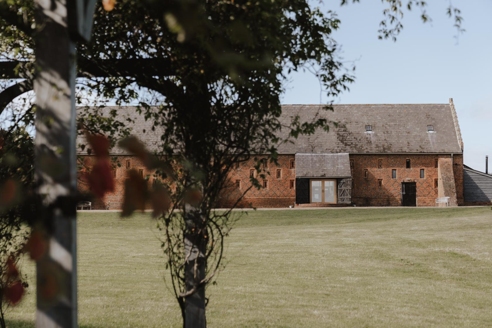 A historic hall with red brick walls and large wooden doors surrounded by open grassy grounds at Copdock Hall.