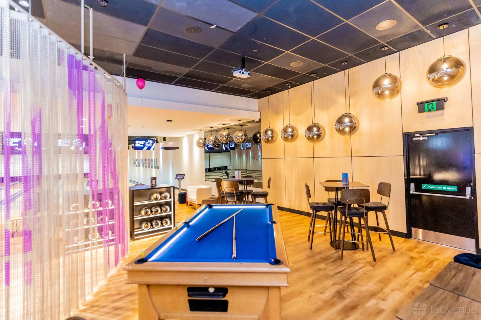 An event venue with a blue felt pool table, modern pendant lights, and high tables at Kingpin Norwood.