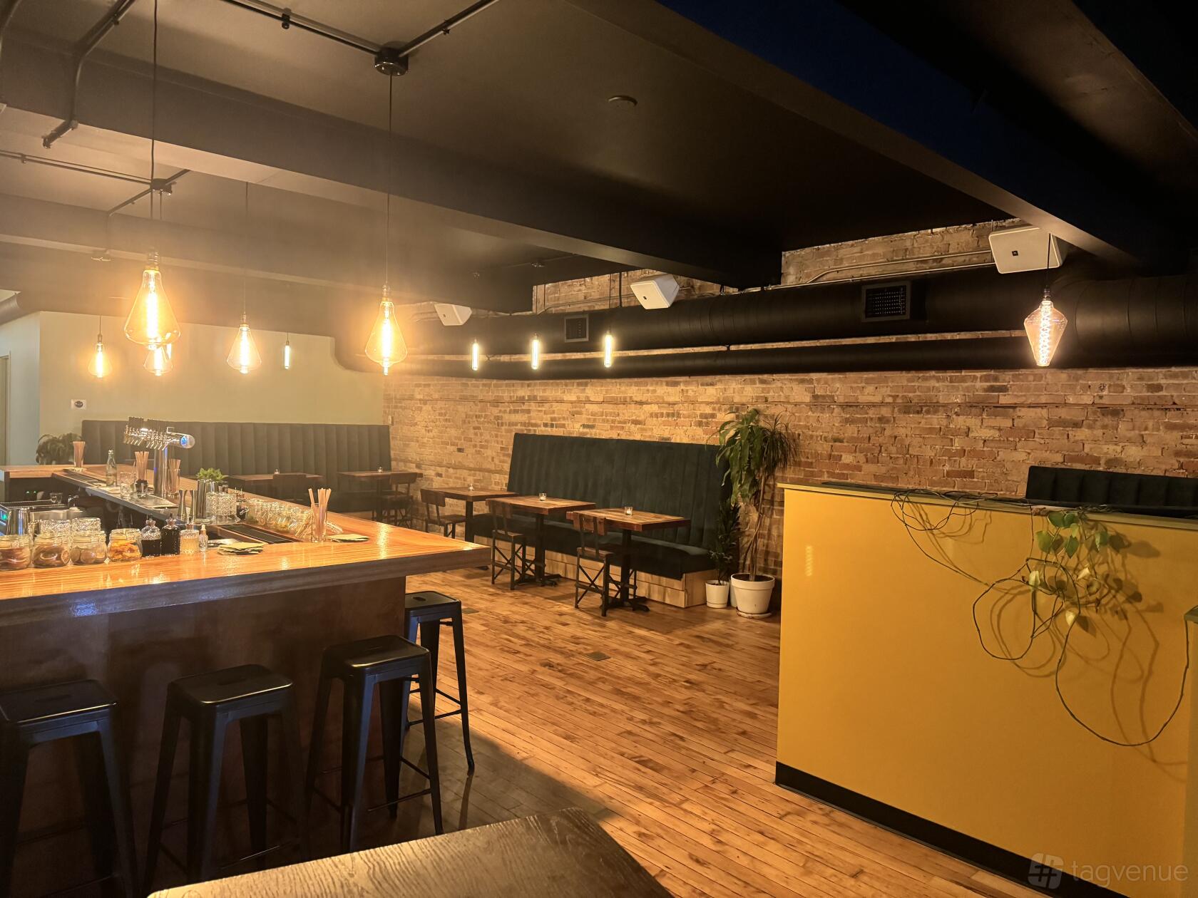 A cocktail bar with exposed brick walls, pendant lighting, and a wooden bar counter at Clara Chicago.