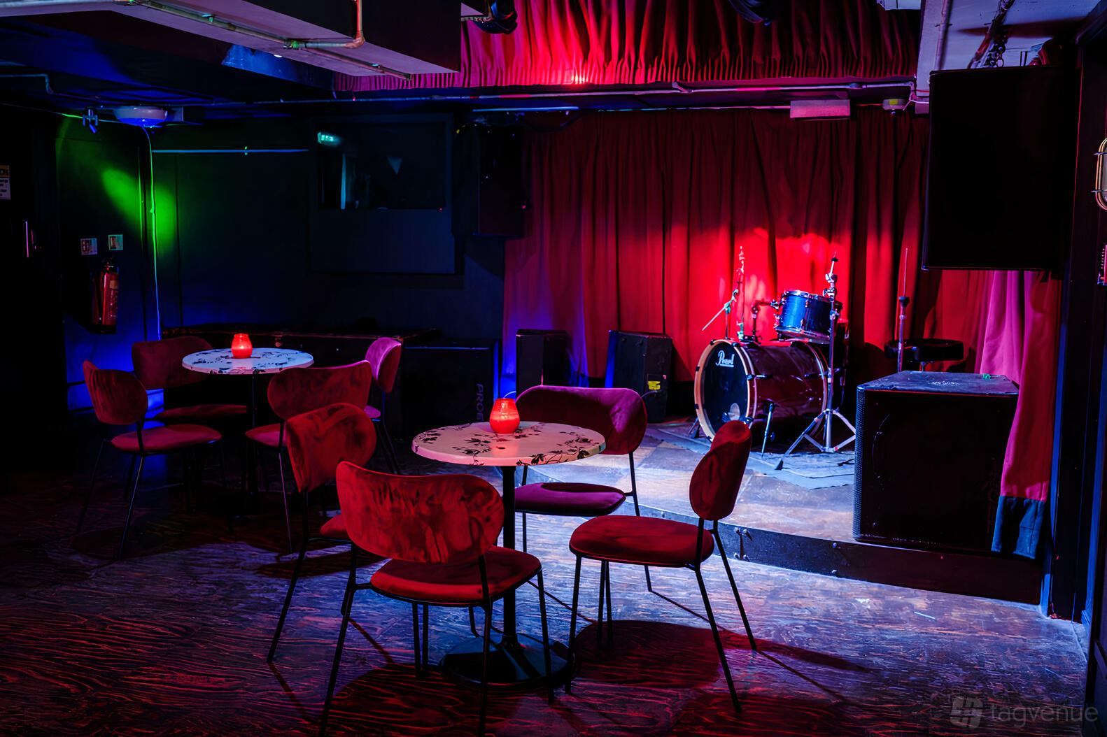 A live music venue with a small stage, drum kit, red velvet curtains, and round tables at The Star in Shoreditch.