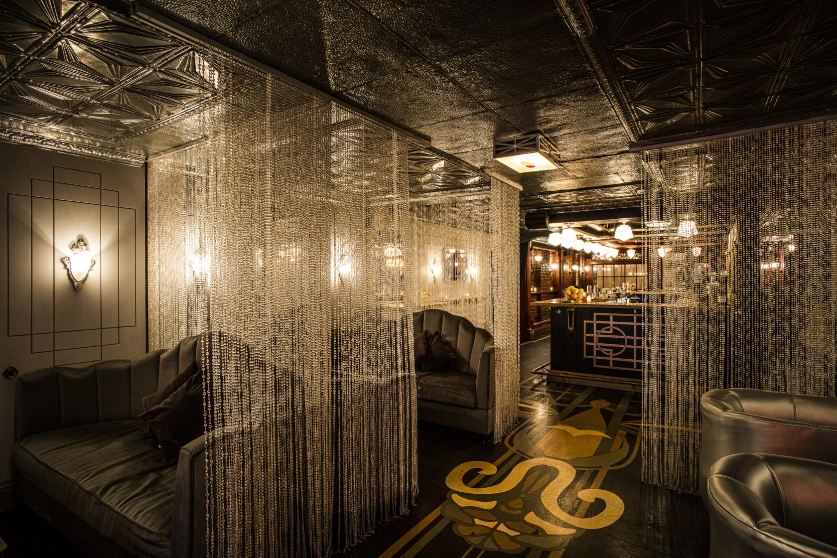 A cocktail bar with velvet booths, metallic bead curtains, and art deco lighting at Dear Irving Gramercy.