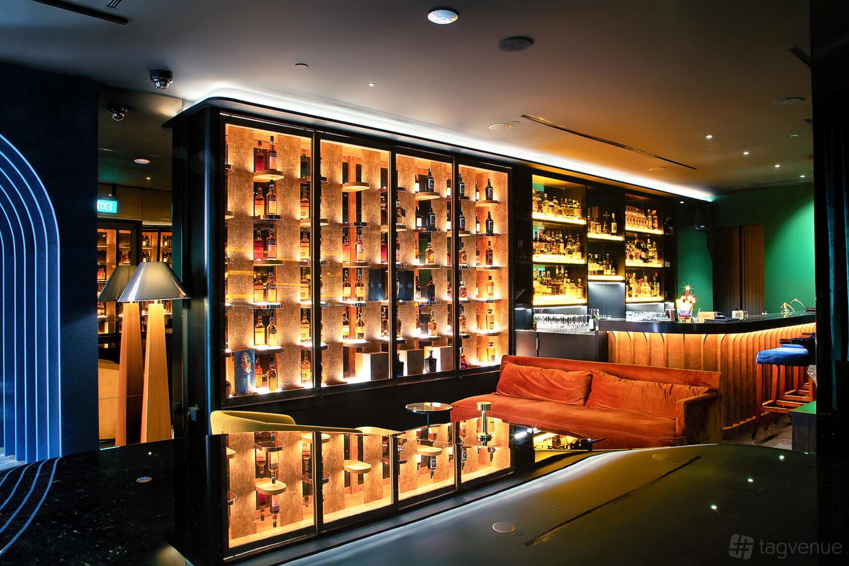 A whisky bar with illuminated bottle display shelves, an orange velvet sofa, and a polished bar counter at Maduro.
