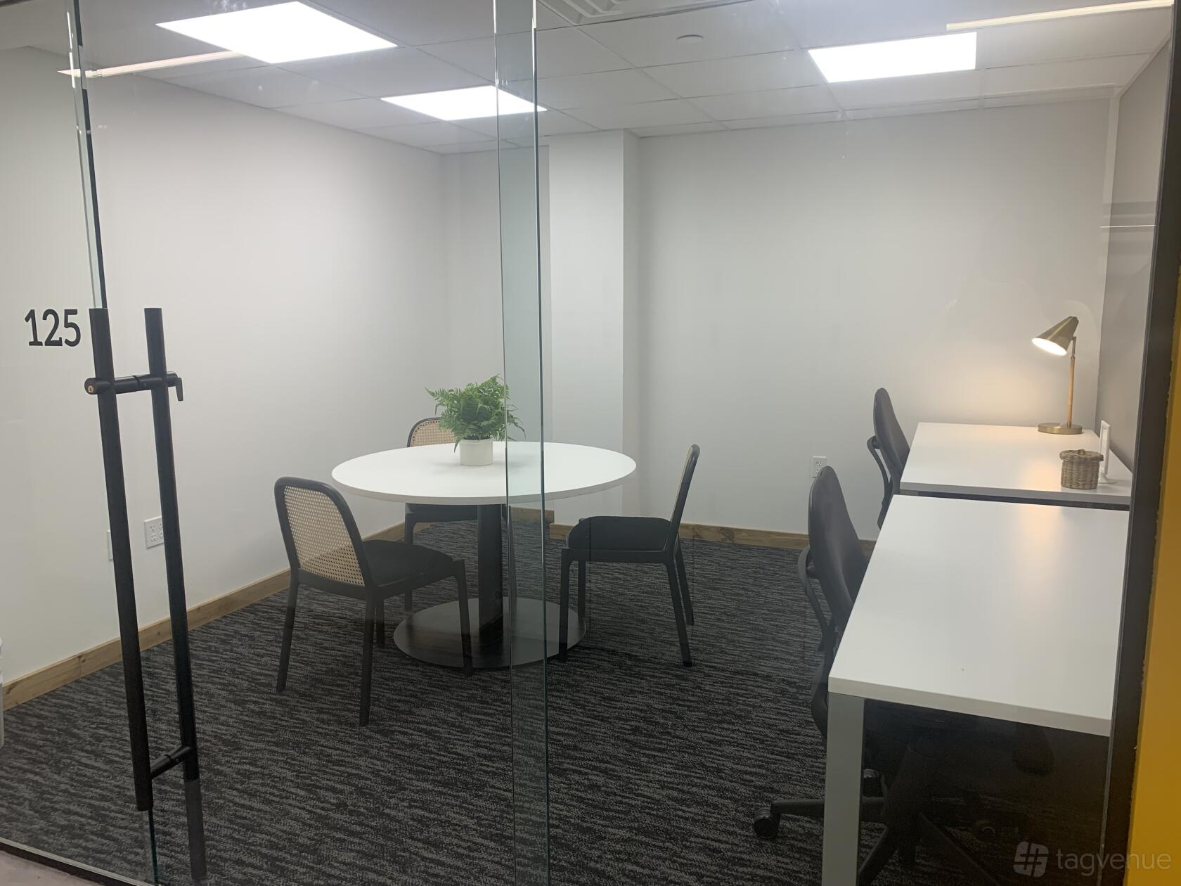 A meeting room with a round table, four chairs, and two white desks with a desk lamp at 25N Coworking Waco.