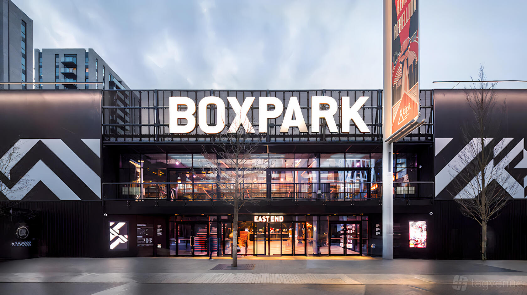 A restaurant with a bold black facade, large illuminated signage, and glass entrance at Boxpark Wembley.