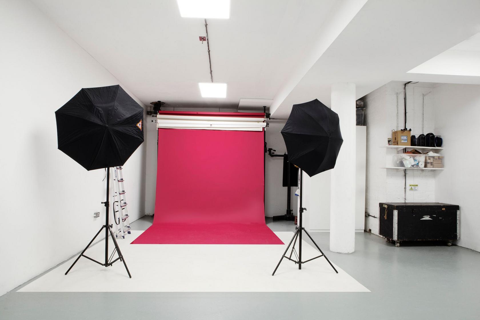 A photo studio with a red backdrop, white walls, and two umbrella lights at Studio 557.