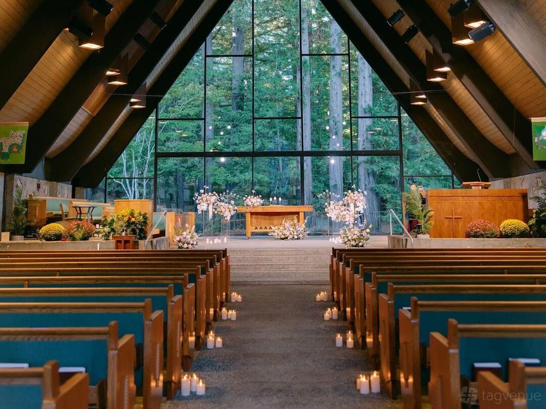 A church interior with wooden pews, high vaulted ceilings, and floor-to-ceiling windows overlooking trees at Valley Presbyterian Church.