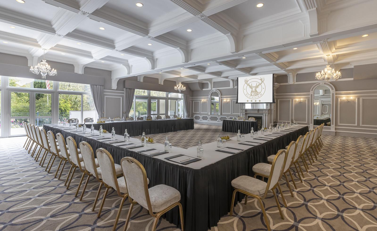 An event space with a U-shaped conference table setup, chandeliers, and large windows at Glenview Hotel & Leisure Club.