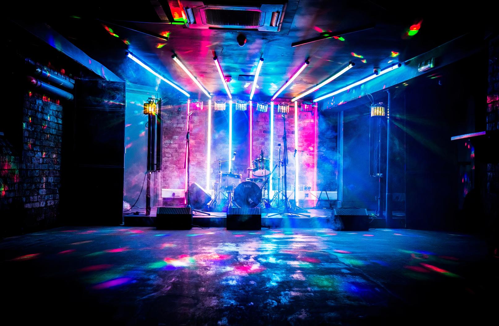 A basement pub event space with exposed brick walls, stage lighting, and a drum kit at The Rainbow Pub.