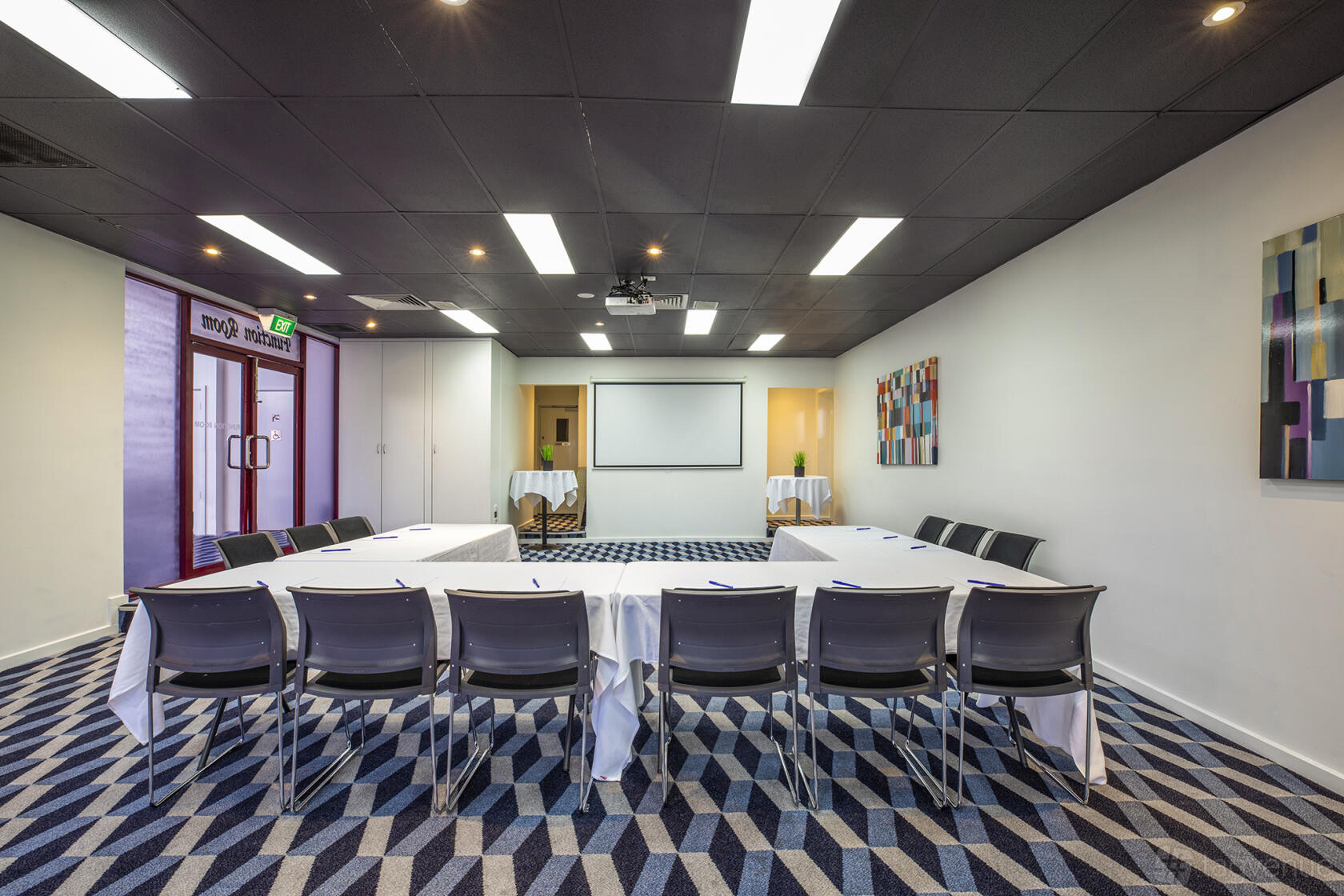 A function room with a U-shaped table setup, geometric carpet, and wall art at Pascoe Vale Hotel.
