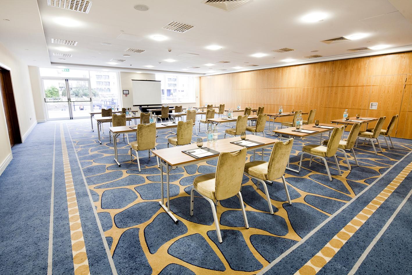 An event space with blue patterned carpet, wood panel walls, and conference tables with chairs at Chelsea Harbour Hotel & Spa.