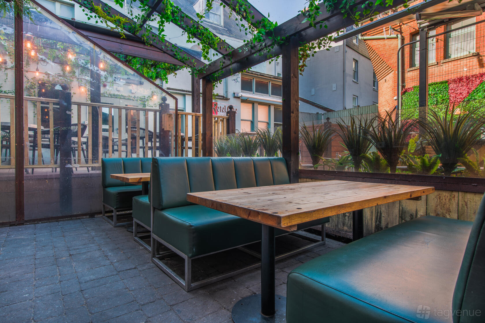 An outdoor bar area with wooden tables, green booth seating, and vine-covered pergola at Revolution Brighton.