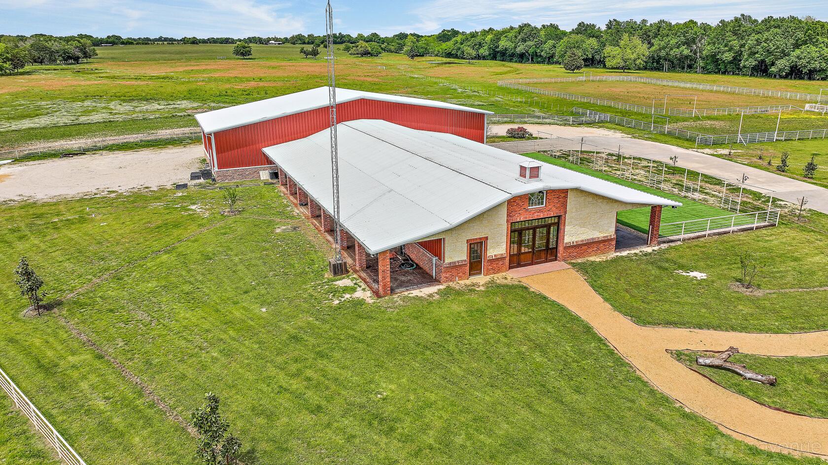 A barn with a large covered entrance, red and beige exterior, and surrounding green fields at The Dream Ranch.