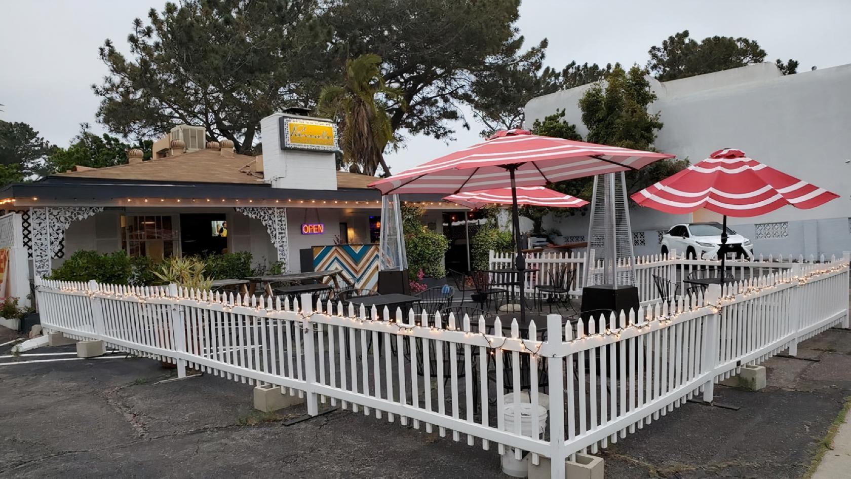 An outdoor restaurant space with red and white umbrellas, string lights, and a white picket fence at Parioli Italian Bistro.
