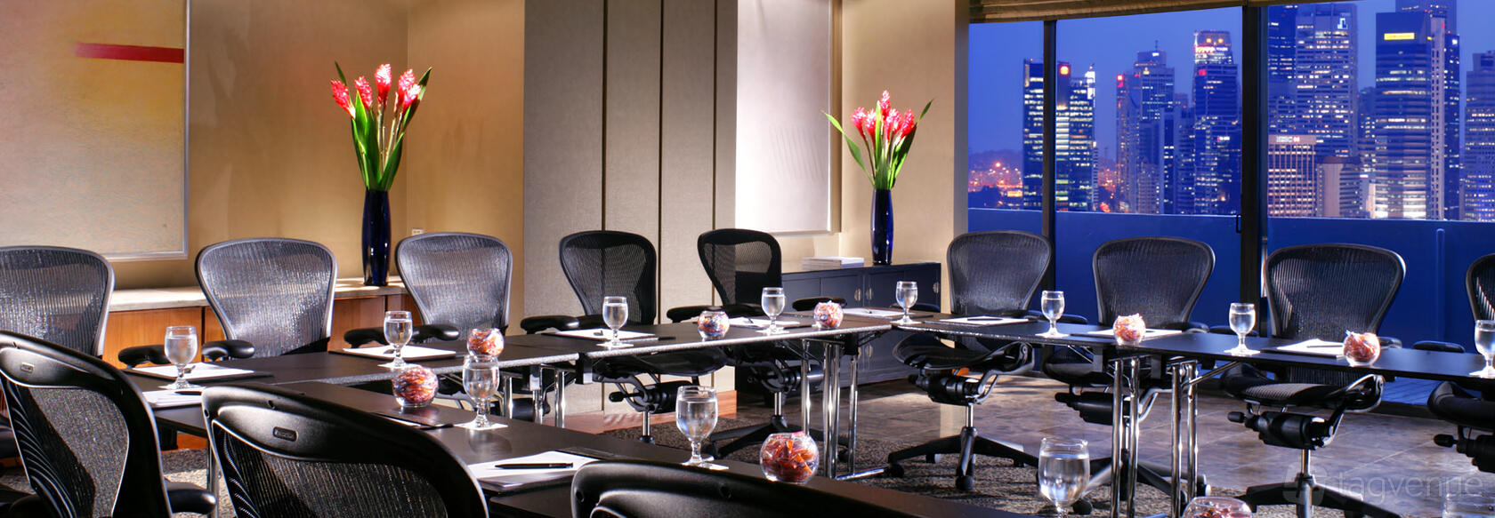 A meeting room with U-shaped tables, ergonomic chairs, water glasses, and floor-to-ceiling windows at Pan Pacific Singapore.