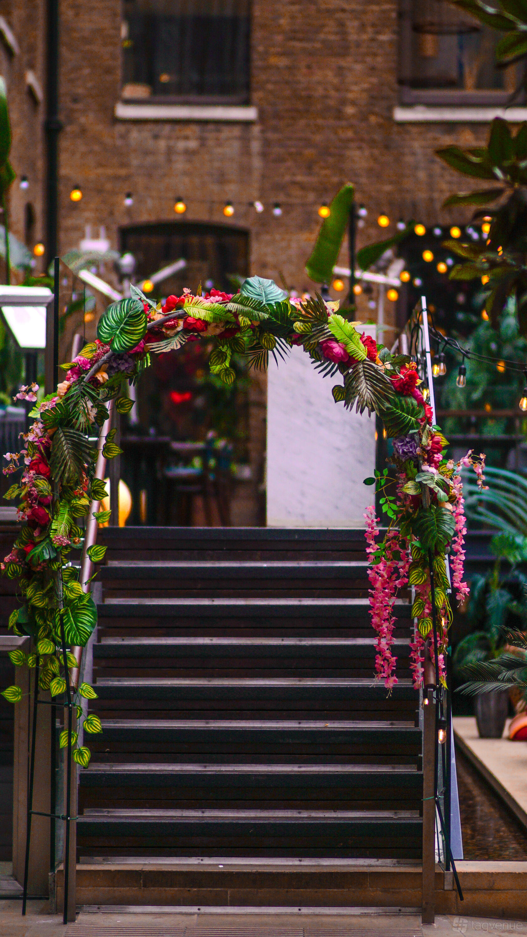 A restaurant with a floral archway over steps, surrounded by plants and brick walls at Cinnamon Kitchen.