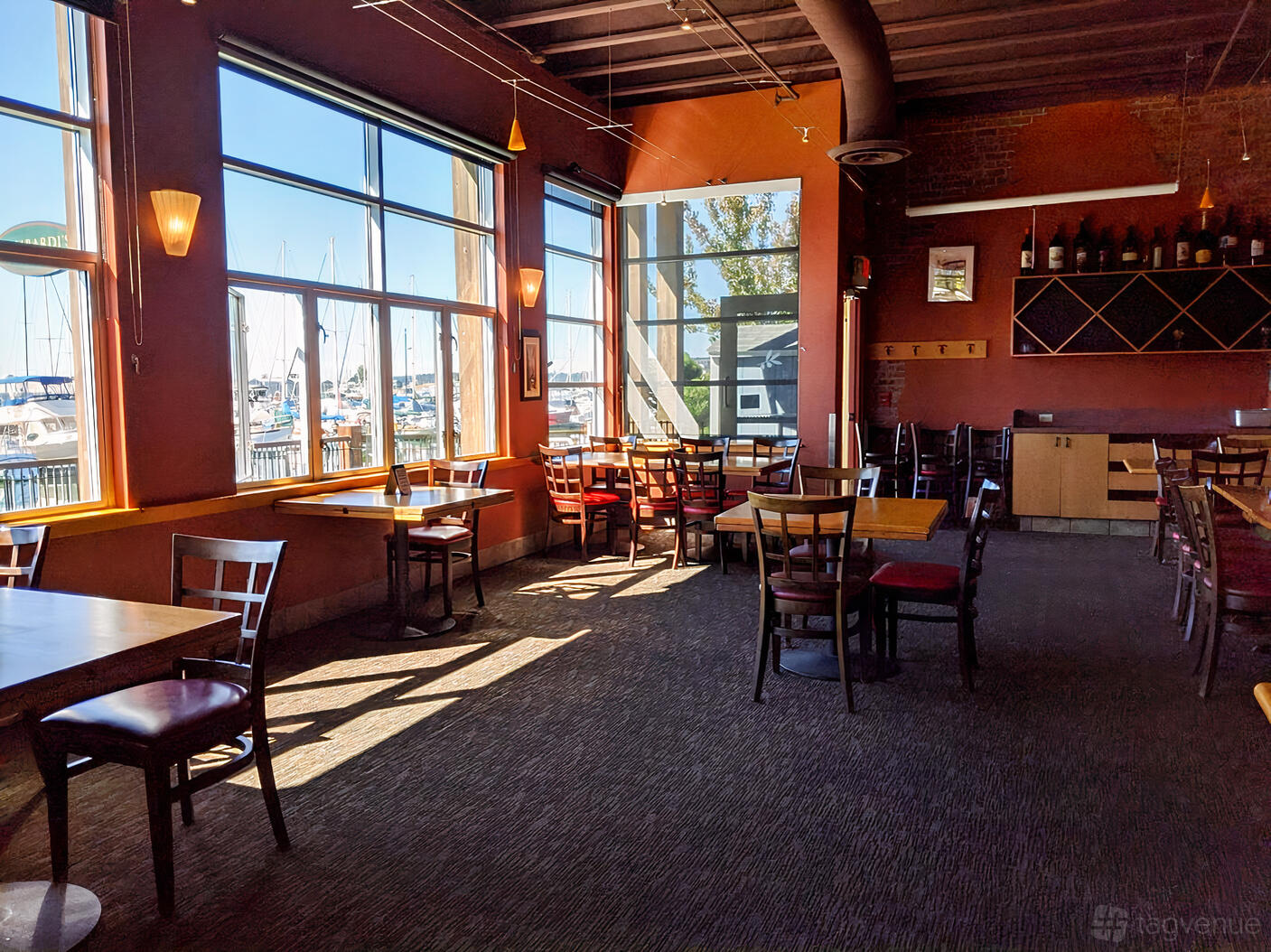A restaurant with large windows overlooking a marina, wooden chairs, and wall-mounted wine racks at Lombardi’s Everett.