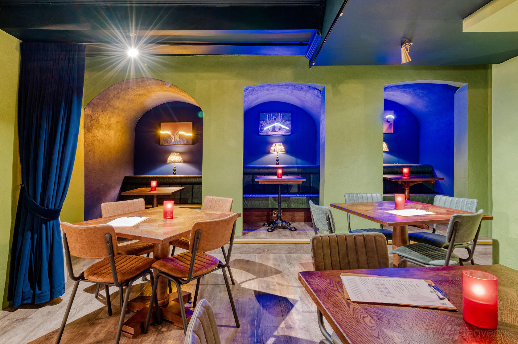 An event space in a pub with arched alcove seating, colorful lighting, and wooden tables at The Albany.