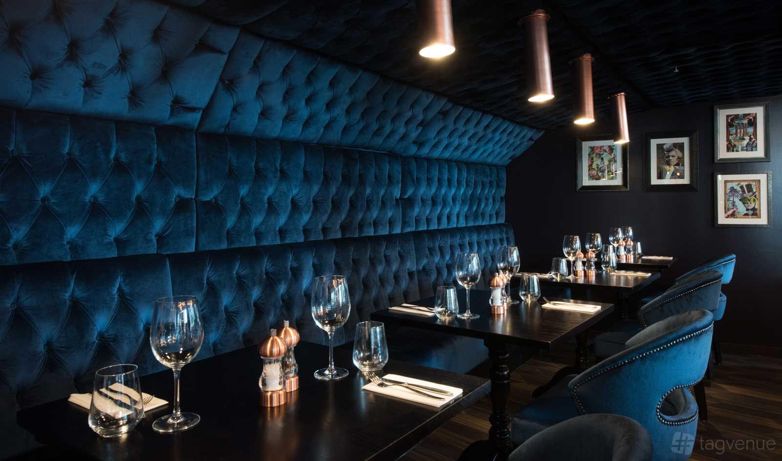A restaurant with blue tufted velvet banquettes, dark wood tables, and pendant lighting at Rocket.