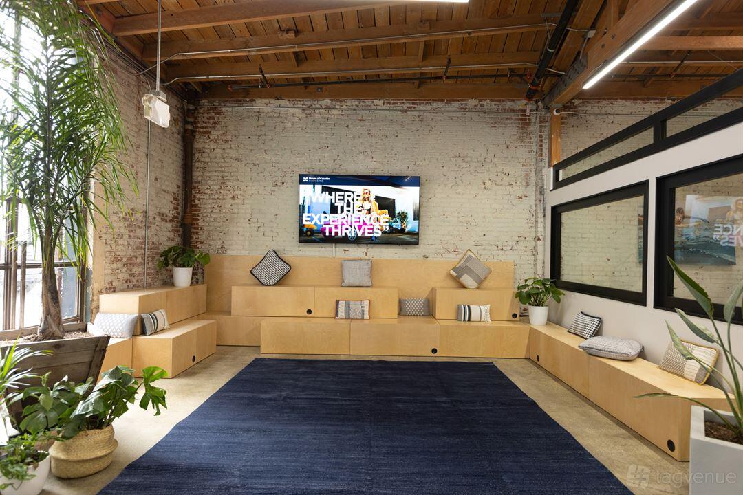 A coworking space with built-in wooden seating, exposed brick walls, large windows, and a mounted TV at House of Cocotte.
