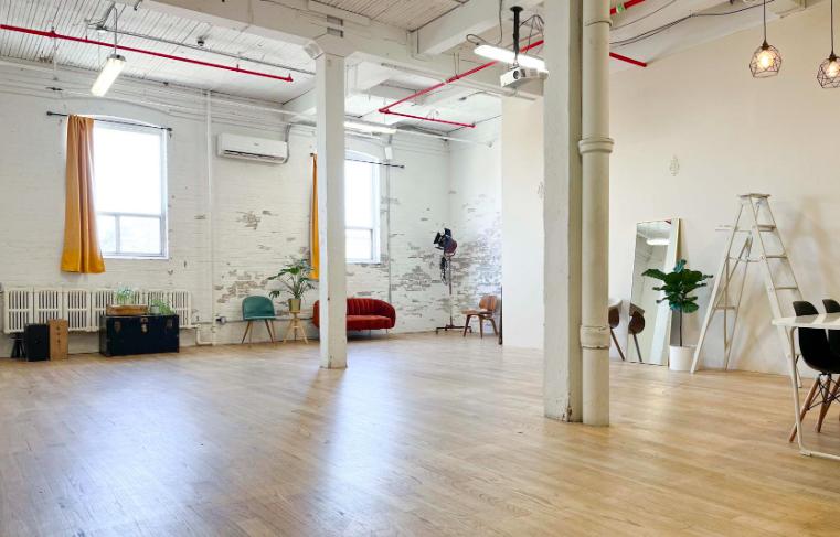 A loft photo studio with large windows, white painted brick walls, wood floors, and studio props at Professional Photography Studio / Wade Studio.
