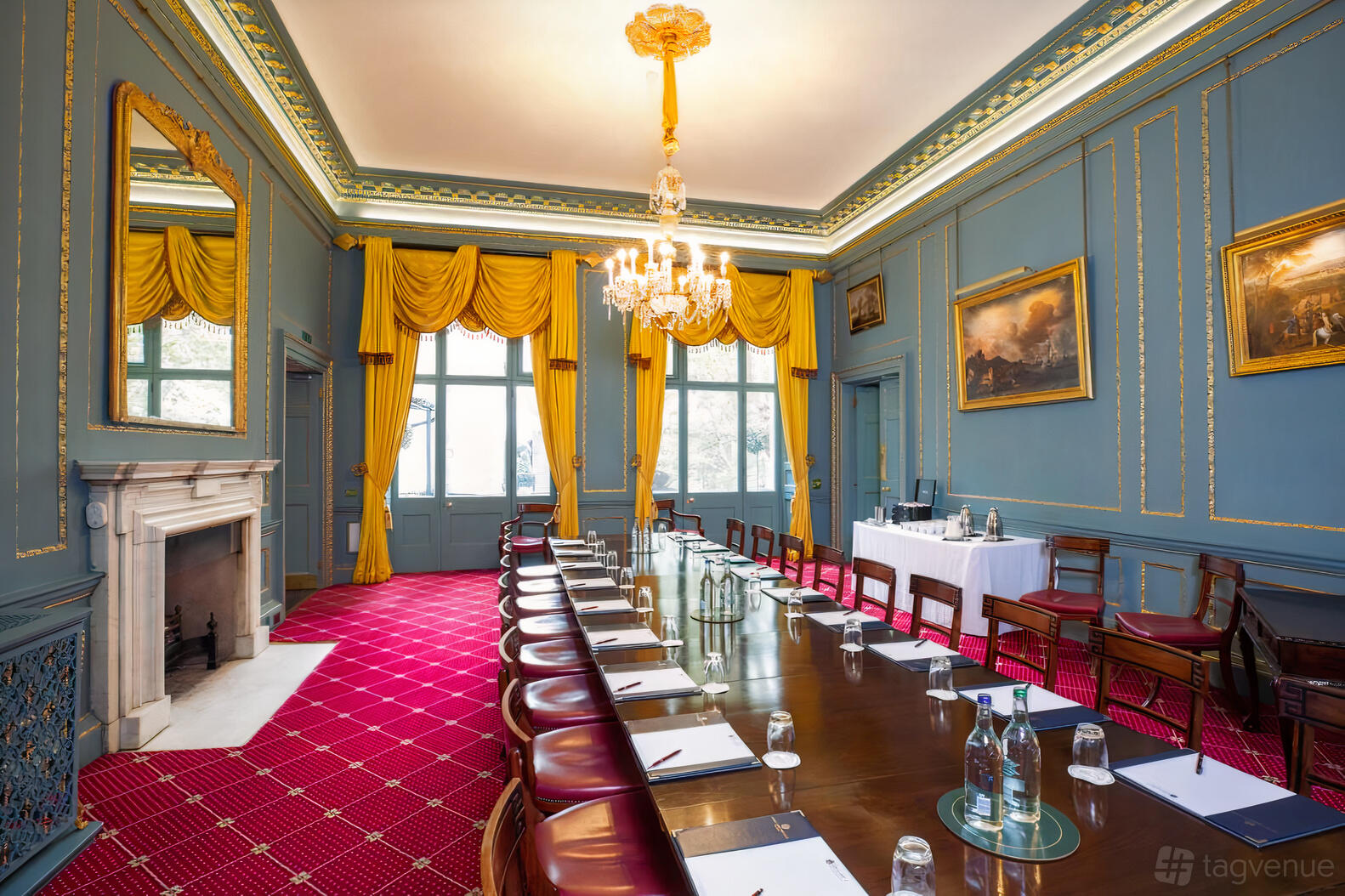 An event space in a bar with blue panelled walls, gold chandeliers, and a long boardroom table at In and Out Club Astor Room.