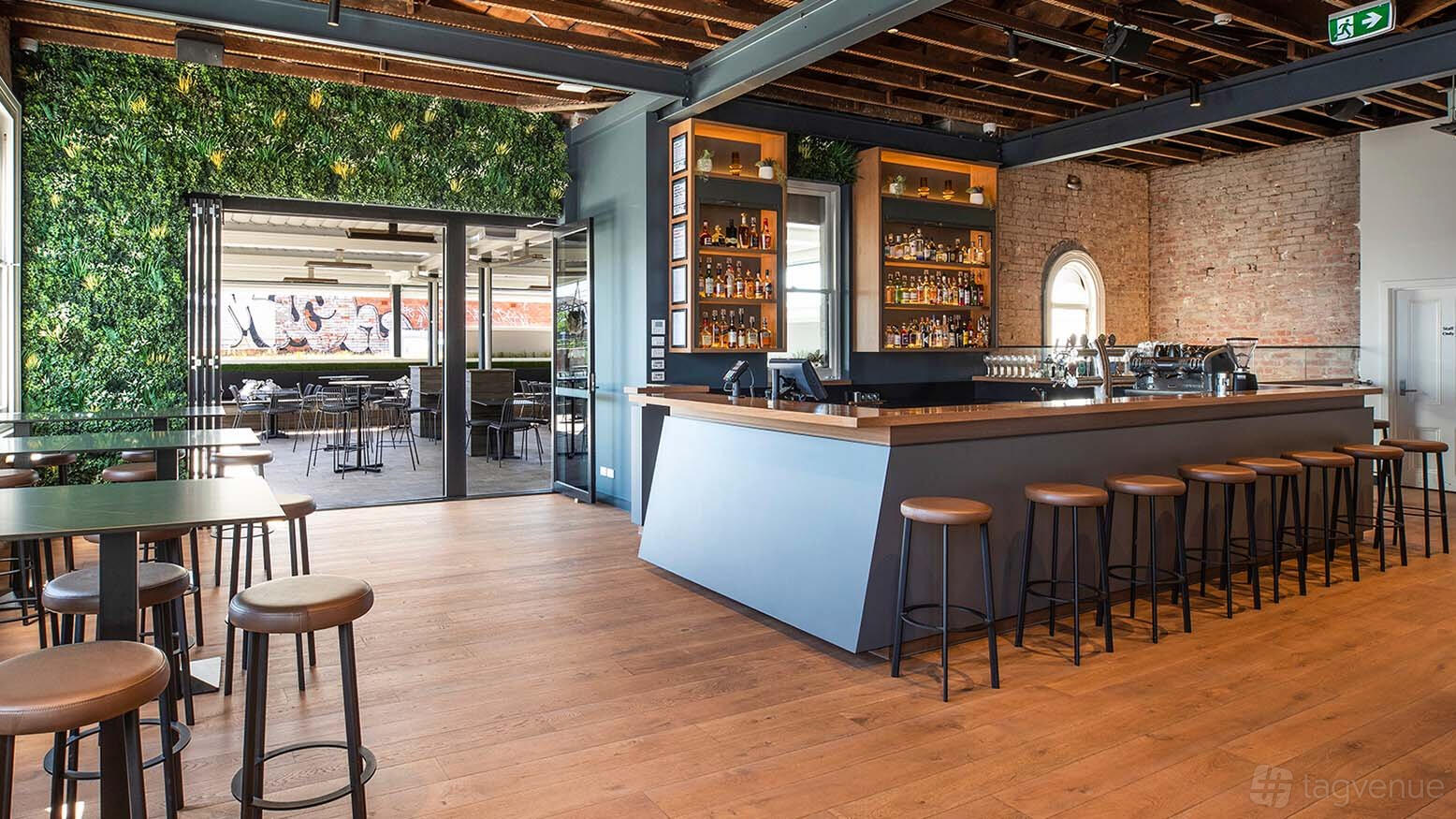 A rooftop bar with exposed brick walls, wooden floors, and a plant-covered accent wall at Balaclava Hotel.