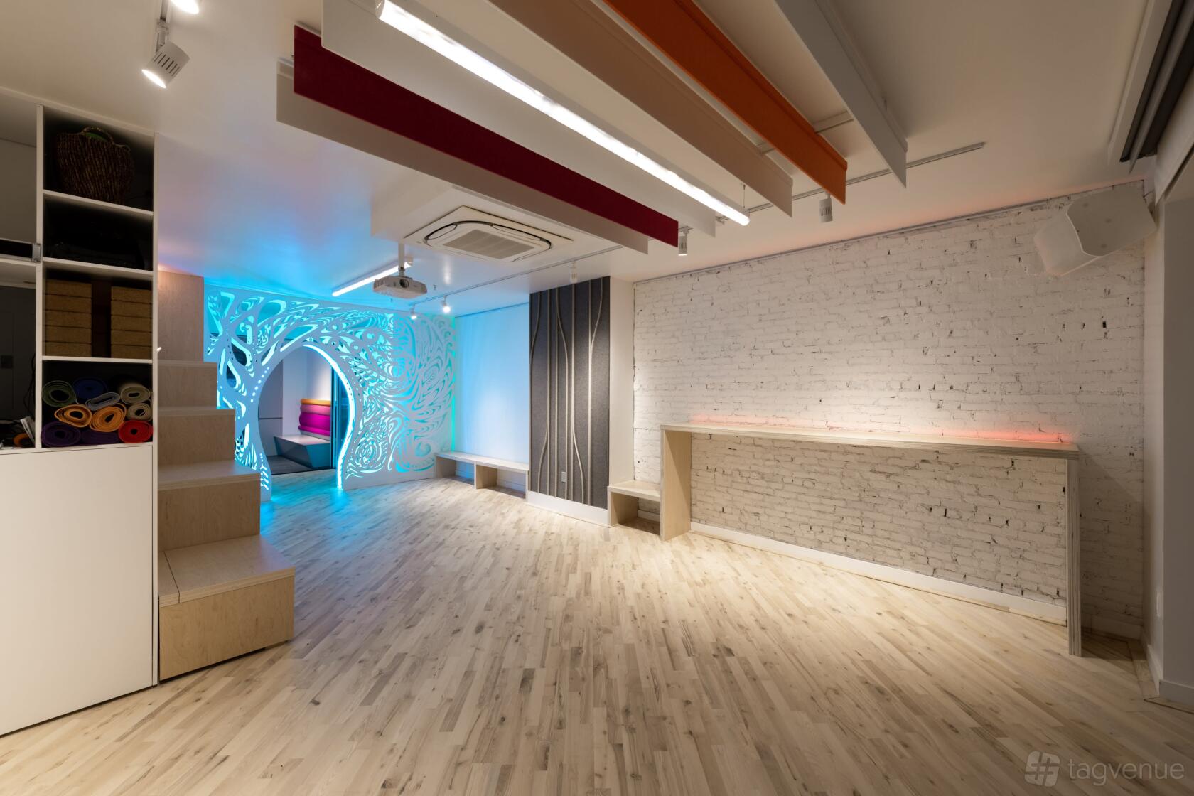 An event venue with white exposed brick walls, light wood floors, and illuminated art installation at Delight Factory NYC.