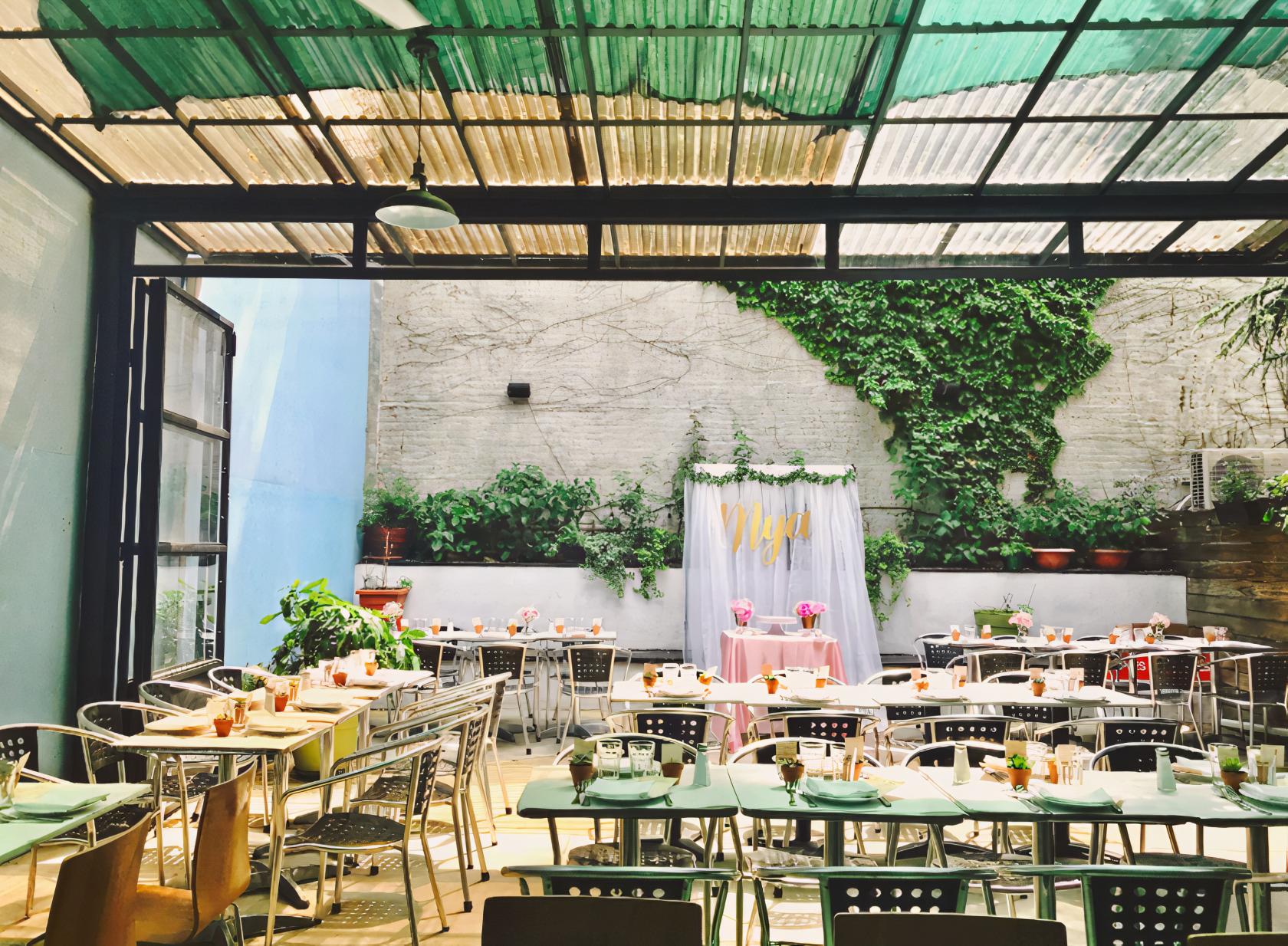 An outdoor restaurant garden with metal chairs, potted plants, and a covered patio at Baci & Abbracci.