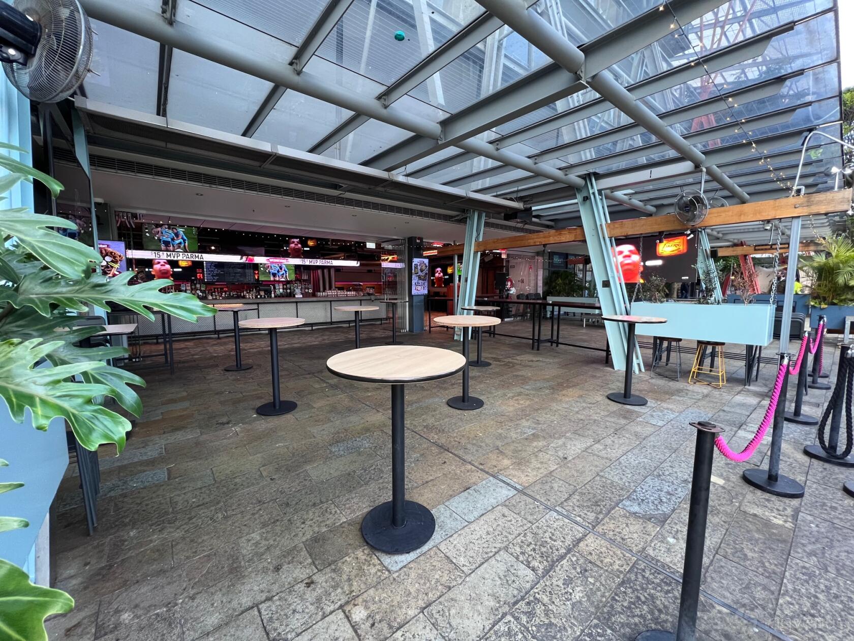 A pub with high ceilings, open-air layout, standing tables, and multiple sports screens at The Sporting Globe King Street Wharf.