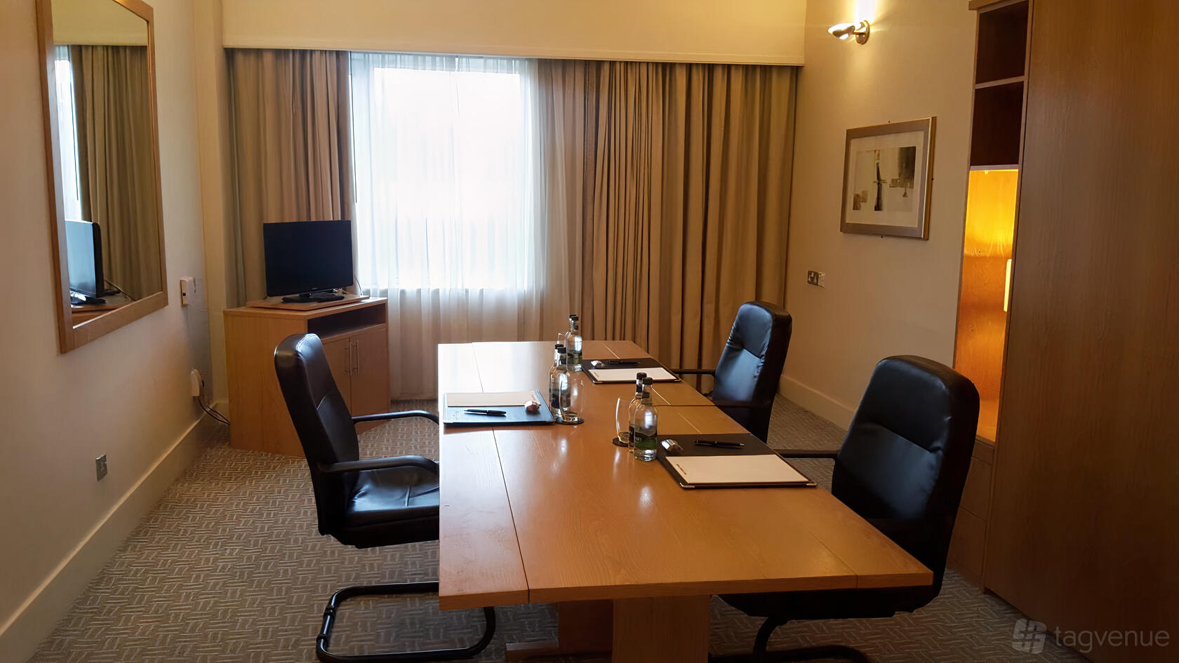 A hotel meeting room with a wooden table, black leather chairs, natural light, and conference supplies at The Croke Park Hotel.