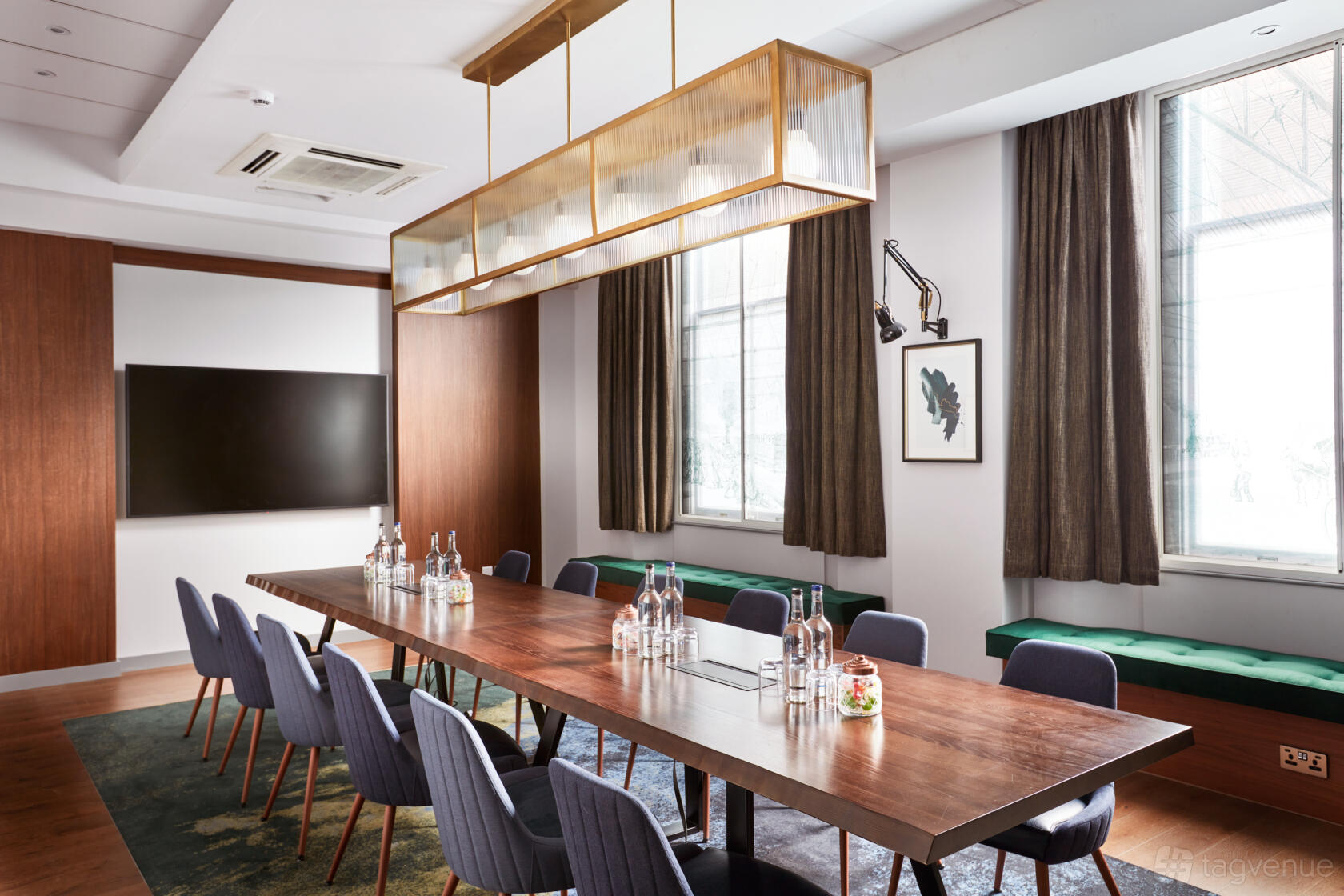 A hotel boardroom with a long wooden table, blue chairs, large windows, and a modern pendant light at The Clermont Victoria.