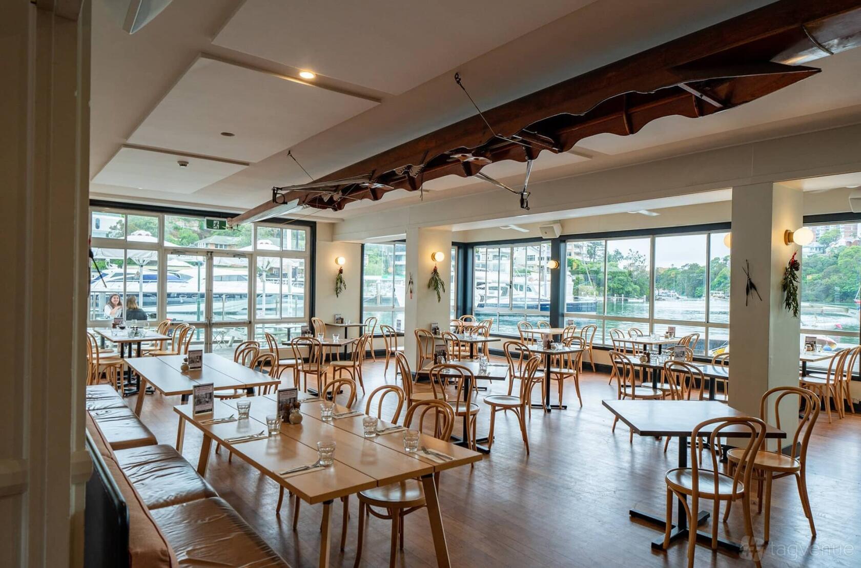 A bar with large windows, bentwood chairs, and natural light overlooking the marina at Mosman Rowers Club.