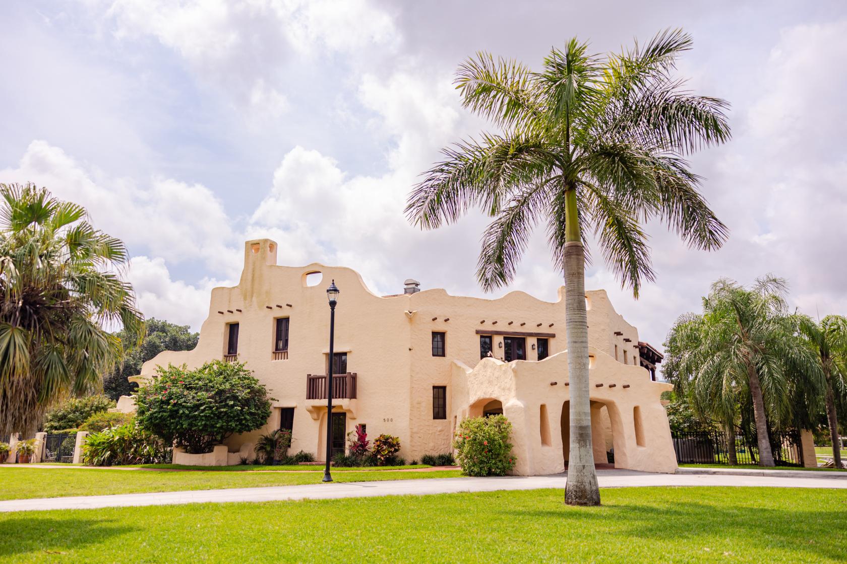 A historic building with stucco walls, arched entryways, and surrounded by palm trees at Curtiss Mansion.