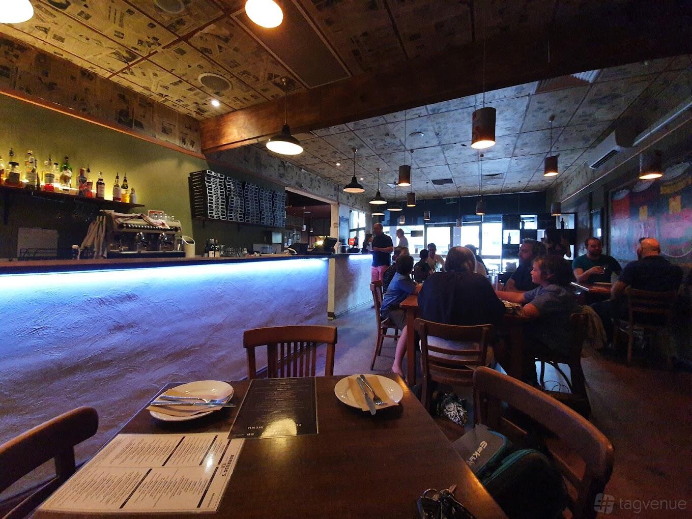 A restaurant with wooden chairs, set tables, and a long bar with blue accent lighting at Borruso's Northbridge.