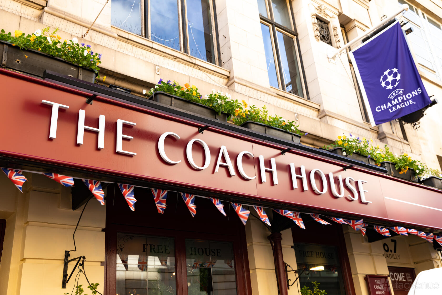 A pub with a deep red exterior sign, flower boxes, and union jack bunting at The Coach House.