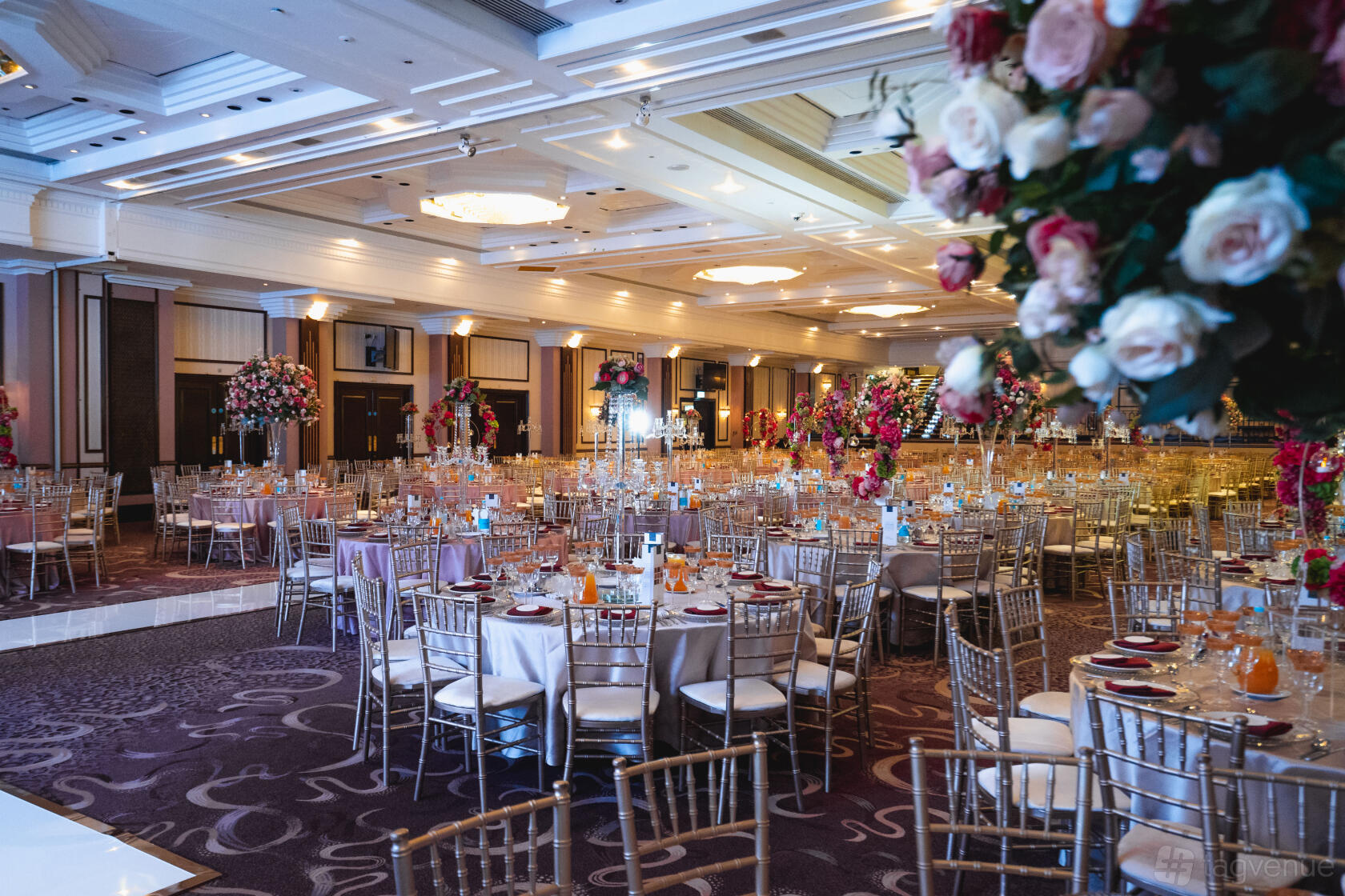 A banquet hall with round tables, gold chairs, floral centerpieces, and decorative ceiling lights at National Motorcycle Museum.