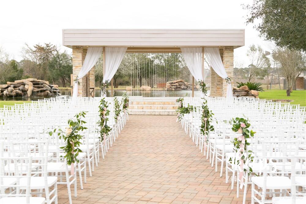 An outdoor ceremony venue with white chairs, draped pergola, and lakeside backdrop at Lindsay Lakes.