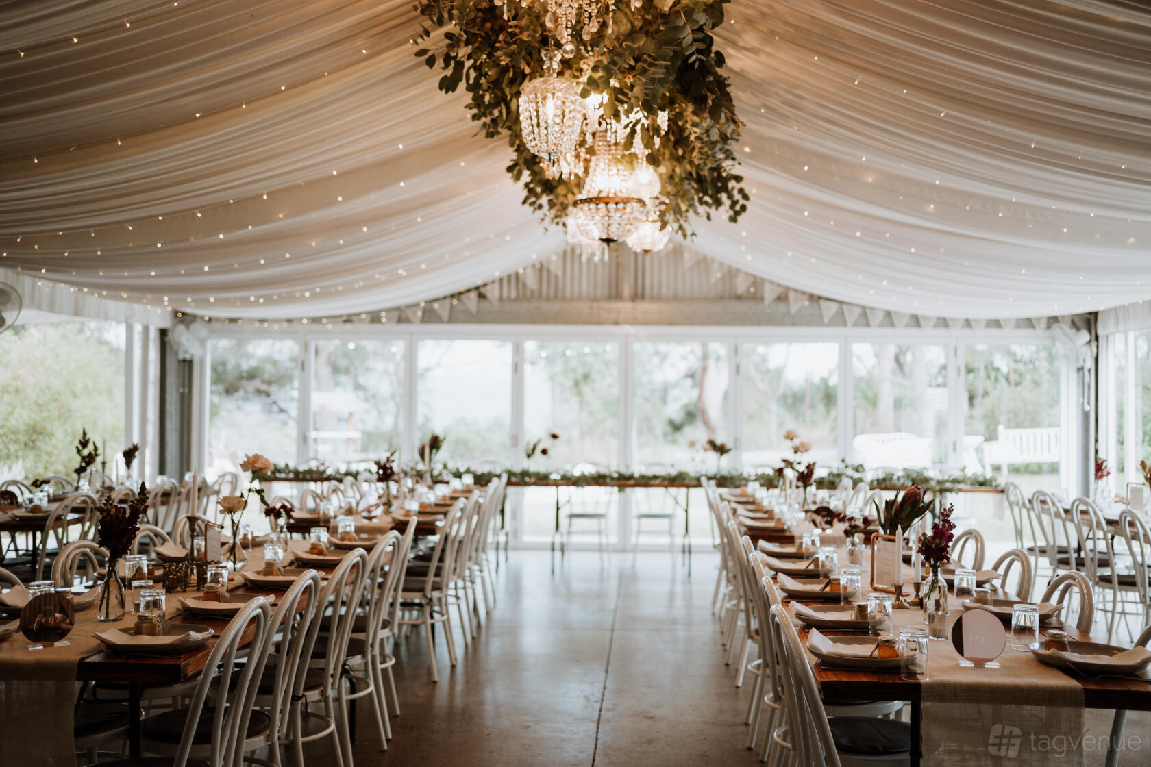 An open air venue with draped ceiling, crystal chandeliers, and long banquet tables at Wildwood Kangaroo Valley.