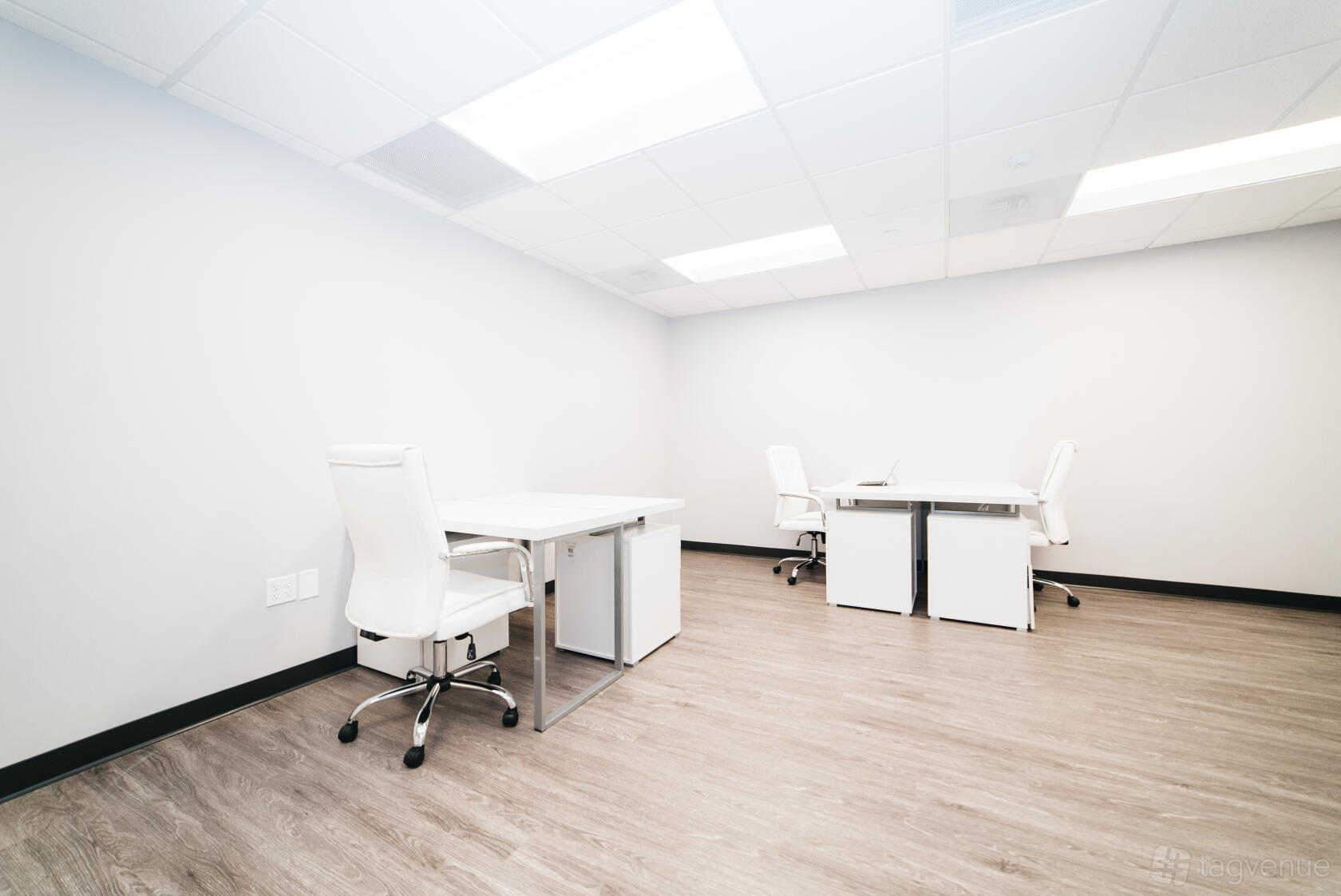 A coworking space with white desks, ergonomic chairs, and wood flooring at Perfect Office Solutions - Fairfax.