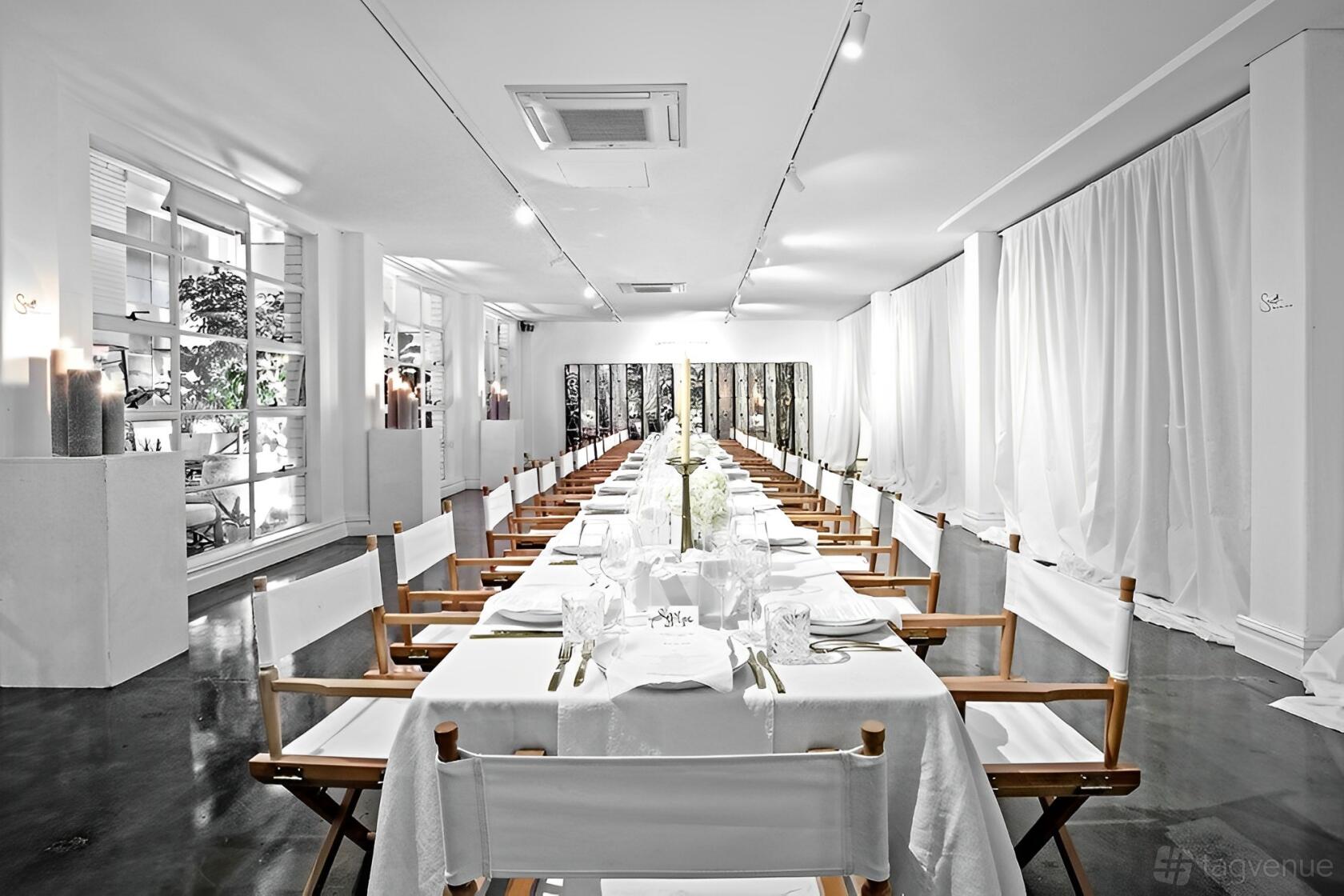 An event venue with floor-to-ceiling white drapes, polished floors, and a long banquet table set for dining at La Porte Space.